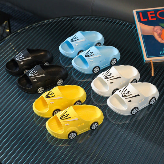 Cartoon kid baby slippers in black, white, yellow, and blue with car design on a table.