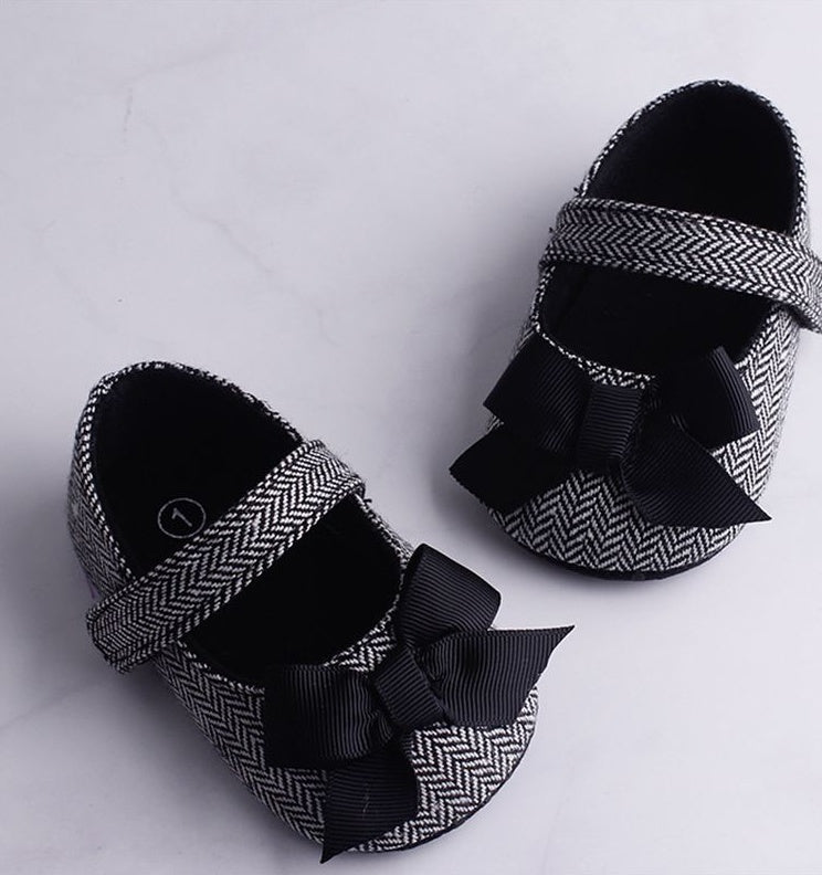 Toddler crib shoes for baby boys with herringbone pattern and black bows.