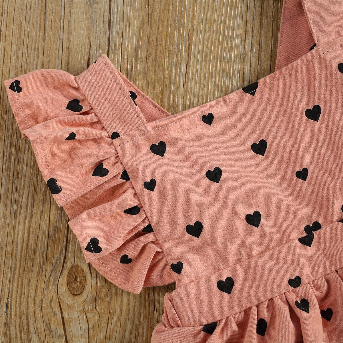 Cute girls' dress with black heart pattern and ruffled sleeves on wooden background.