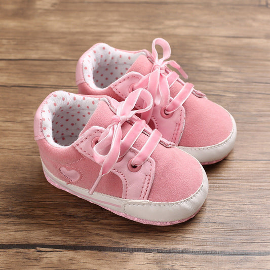 Pink baby sneakers with cotton cloth upper and lace-up design on a wooden surface.
