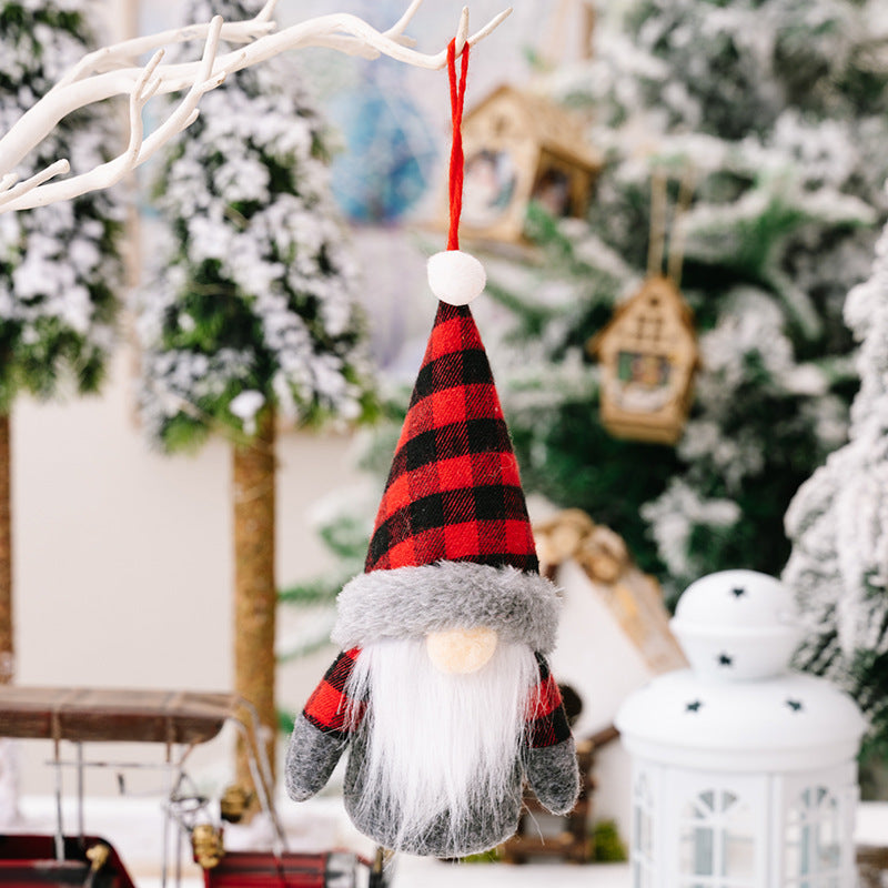 Faceless Christmas doll ornament with red and black plaid hat hanging on a tree branch.