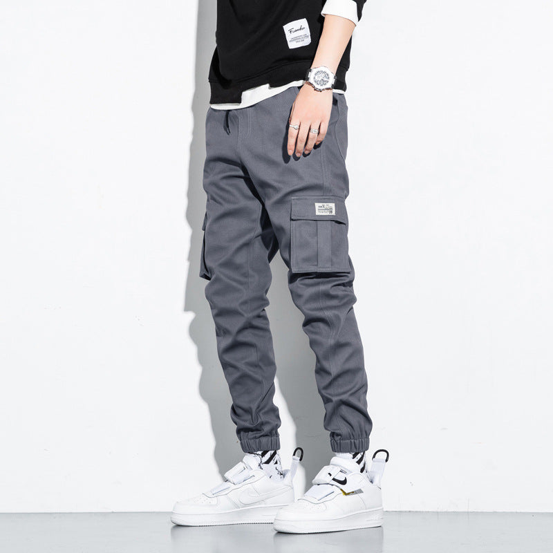 Mens Cotton Cropped Trousers in Grey on a model, showing cargo-style side pockets and tapered legs with white trainers