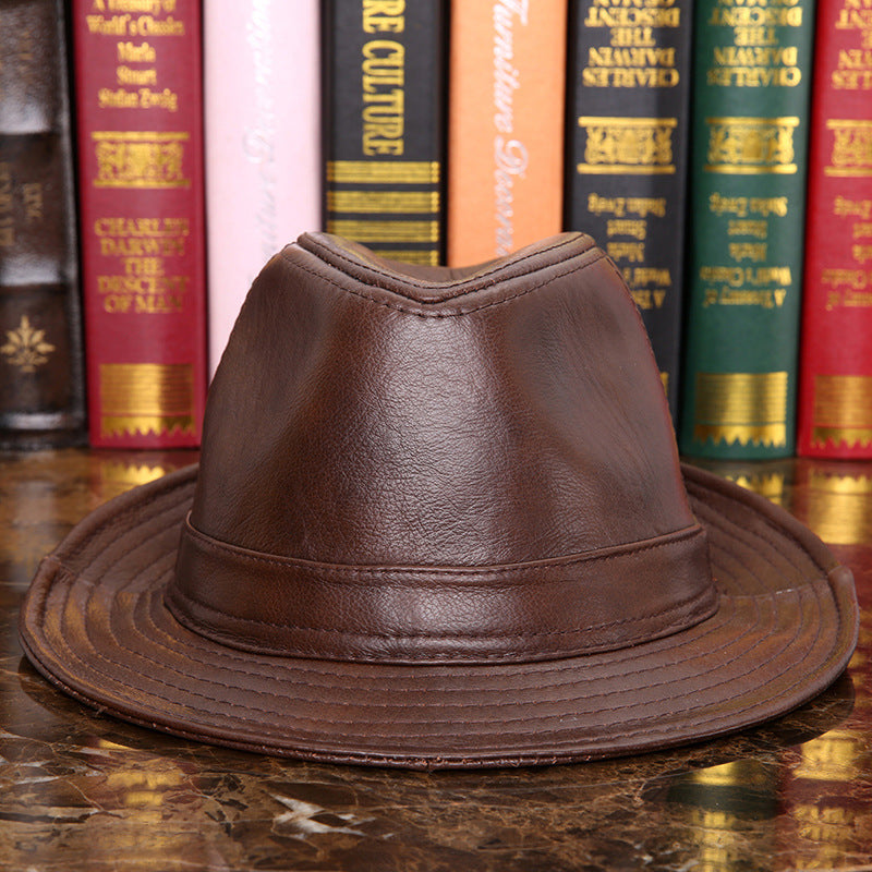 Mens Leather Fedora Hat in Brown, front view on a marble surface with books behind, showing the shaped crown, matching hatband and stitched brim