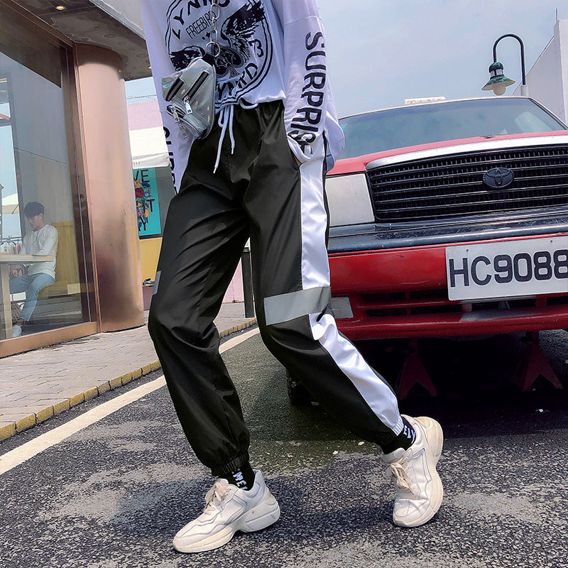 Mens Reflective Track Pants in Black on a model beside a red car, showing the side panels and gathered ankle finishes
