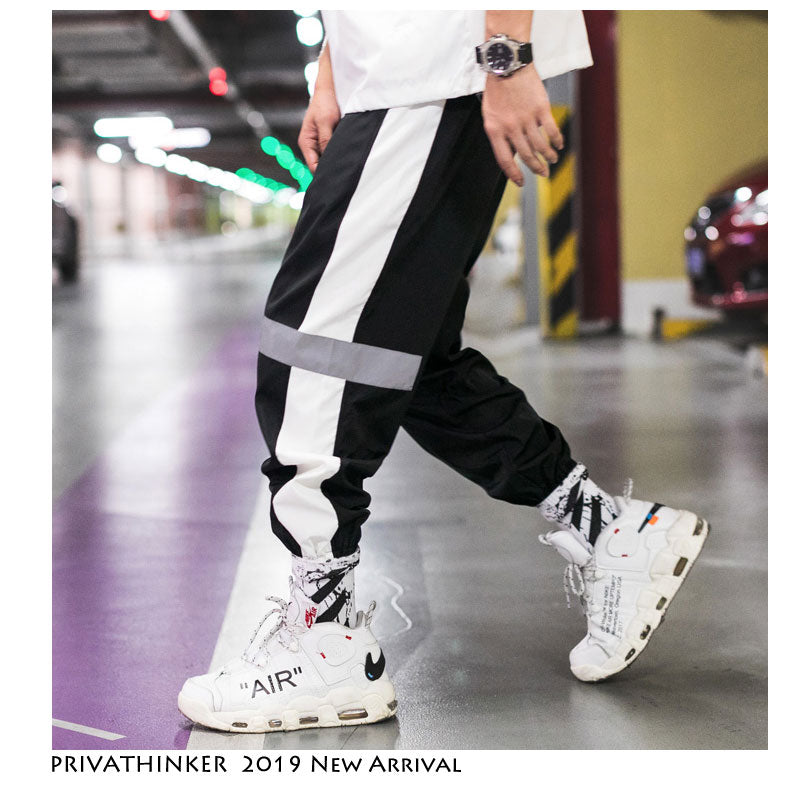 Mens Reflective Track Pants in Black & white on a model indoors, showing contrasting side panels and gathered ankles with white trainers