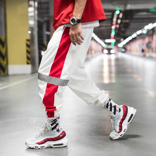 Mens Reflective Track Pants in White on a model, showing red side panels, reflective bands and gathered ank