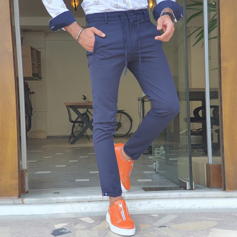 Mens Straight Casual Trousers in navy blue, model posing outside an entrance with one leg crossed and orange trainers