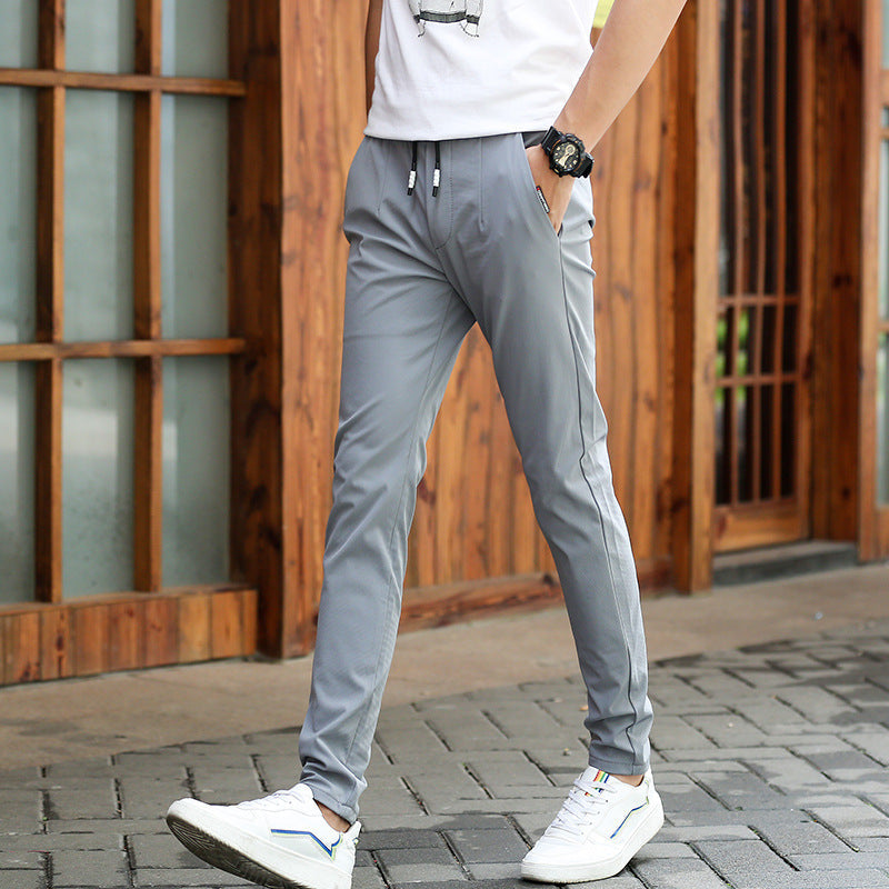 Mens Thick Stretch Trousers in Gray on a model outdoors beside a wooden building, styled with a white T-shirt and white trainers