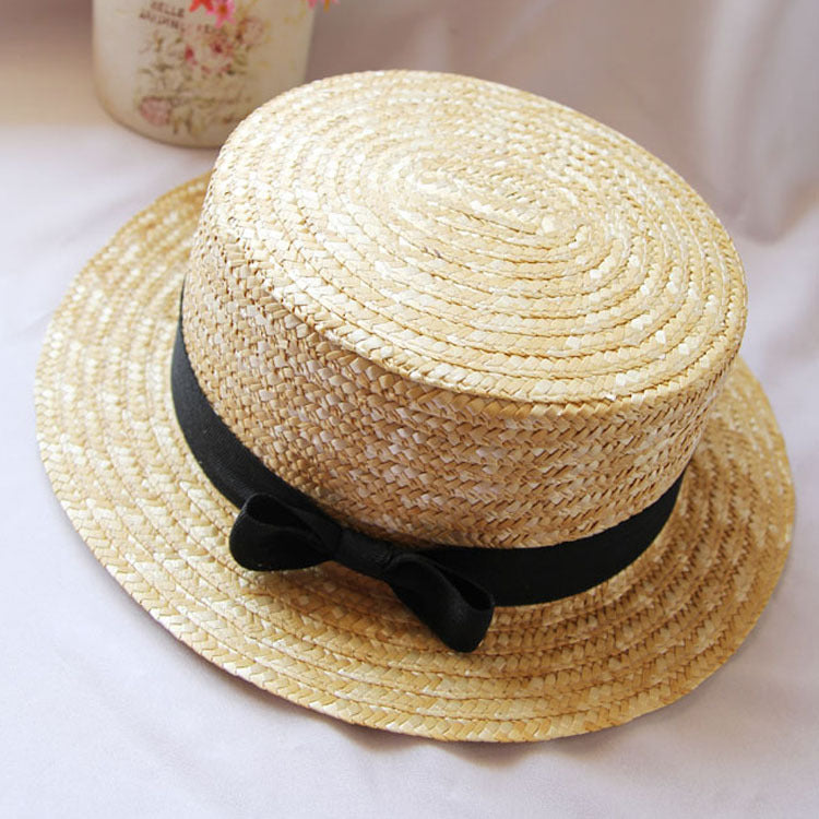 Womens Boater Straw Hat in natural straw tones with a flat crown and black ribbon tied into a bow.