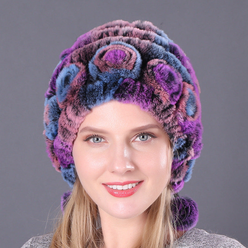 Womens Rabbit Fur Hat in purple, pink and blue tones with floral details and hanging pom-poms, worn by a smiling model.