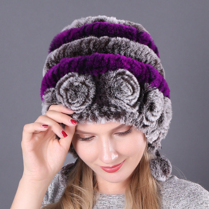 Womens Rabbit Fur Hat with purple and grey stripes, grey floral details and hanging pom-poms, worn by a model looking down.